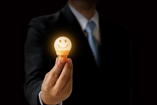 Businessman hand give the smile face emoticon on the light buld to increase rating of products and services concept, Customer service and business satisfaction survey,selective focus.