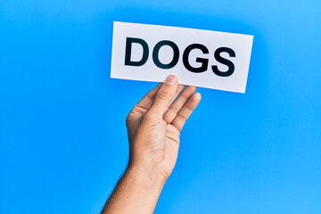 Hand of caucasian man holding paper with dogs word over isolated blue background