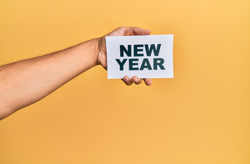 Hand of caucasian man holding paper with new year message over isolated yellow background