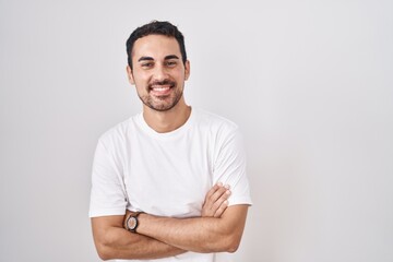 Handsome hispanic man standing over white background happy face smiling with crossed arms looking...