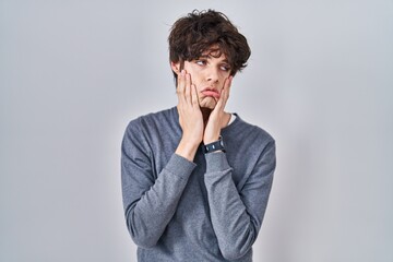 Young man standing over isolated background tired hands covering face, depression and sadness, upset and irritated for problem