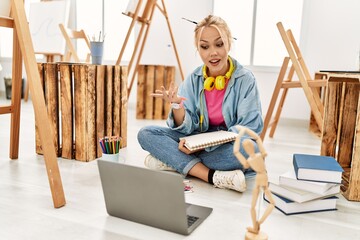 Young caucasian woman artist having video call sitting on floor at art studio