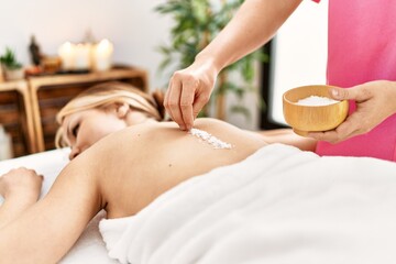 Obraz na płótnie Canvas Young caucasian woman lying on table having back massage using salt at beauty salon