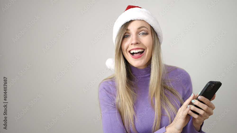 Poster young blonde woman wearing christmas hat using smartphone over isolated white background