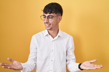 Young hispanic man standing over yellow background smiling showing both hands open palms,...