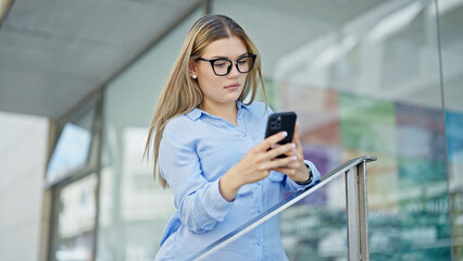 Young blonde woman business worker using smartphone with serious expression at street