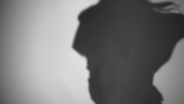 Dancing in the shadows. Silhouette of a girl dancing hip-hop. A person who loves dancing. Shadow on the white wall. The girl dances coolly, a shadow on the wall from the light