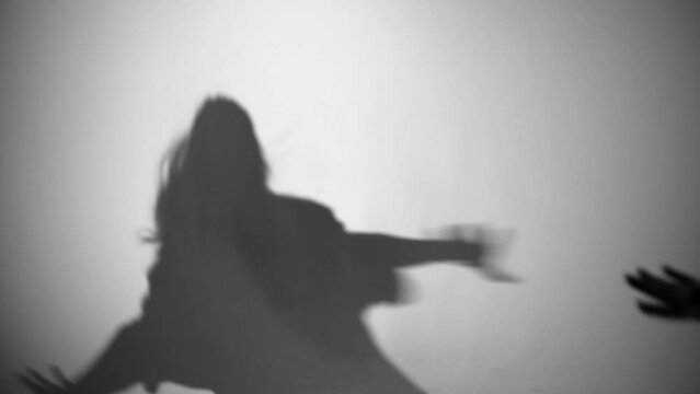 Dancing in the shadows. Silhouette of a girl dancing hip-hop. A person who loves dancing. Shadow on the white wall. The girl dances coolly, a shadow on the wall from the light