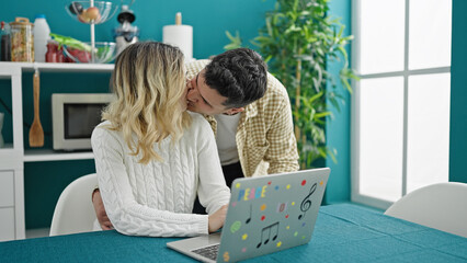Man and woman couple sitting on table using laptop kissing at dinning room