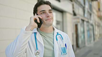 Young hispanic man doctor smiling confident talking on smartphone at hospital