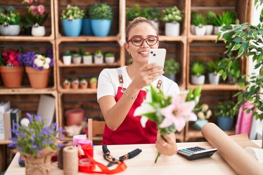 Young beautiful hispanic woman florist make photo to flower by smartphone at florist