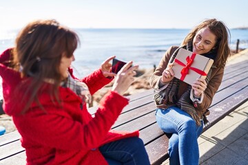 Two women mother and daughter make photo by smartphone holding gift at seaside