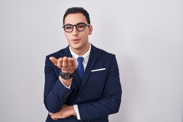 Young hispanic man wearing suit and tie looking at the camera blowing a kiss with hand on air being lovely and sexy. love expression.