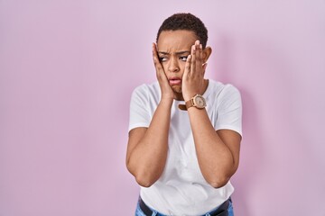 Beautiful african american woman standing over pink background tired hands covering face, depression and sadness, upset and irritated for problem