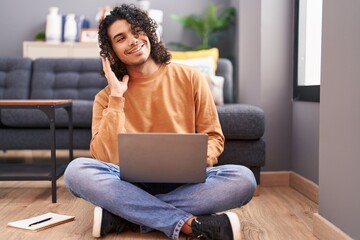Young latin man listening to music sitting on floor at home