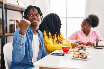 Fototapeta na wymiar Group of three young black people sitting on a table having coffee pointing thumb up to the side smiling happy with open mouth