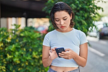 Young hispanic woman using smartphone with relaxed expression at street