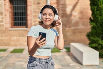 Young hispanic woman smiling confident listening to music at street