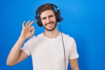 Hispanic man with beard listening to music wearing headphones smiling positive doing ok sign with...