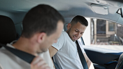 Two men couple sitting on car wearing belt at street