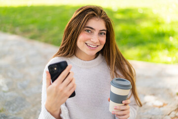 Young pretty caucasian woman using mobile phone and holding a take away coffee