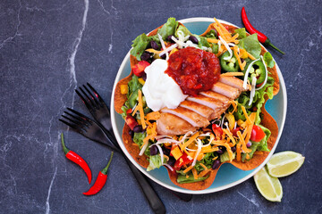 Chicken taco salad with sour cream and salsa. Mexican food dish. Above view table scene on a dark stone background.