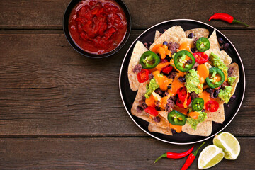 Fully loaded nachos with beef and cheese. Mexican food dish. Overhead view table scene on a dark wood background. Copy space.
