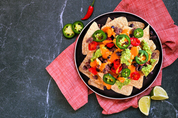 Fully loaded nachos with beef and cheese. Mexican food dish. Above view table scene on a dark slate background.