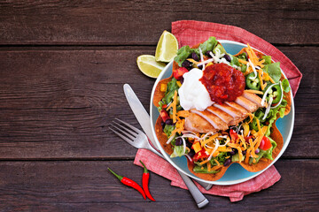 Chicken taco salad with sour cream and salsa. Mexican food dish. Above view table scene on a dark wood background.