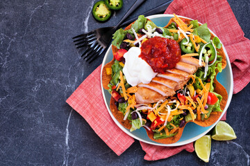 Chicken taco salad with sour cream and salsa. Mexican food dish. Top view table scene on a dark stone background.