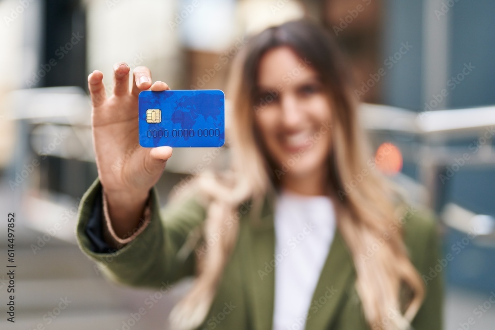 Wall mural Young woman smiling confident holding credit card at street