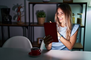 Young hispanic woman using touchpad sitting on the table at night pointing aside worried and...