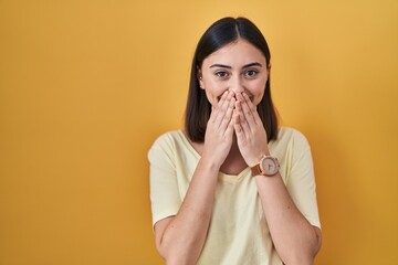 Hispanic girl wearing casual t shirt over yellow background laughing and embarrassed giggle...
