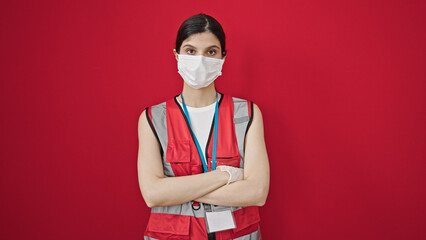 Young beautiful hispanic woman doctor wearing medical mask standing with arms crossed gesture over...