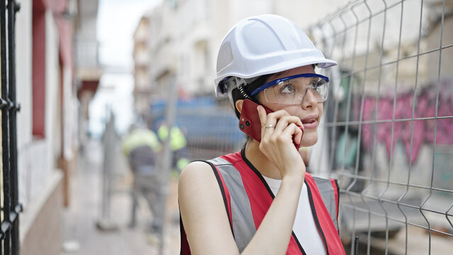 Young beautiful hispanic woman builder talking on smartphone at street