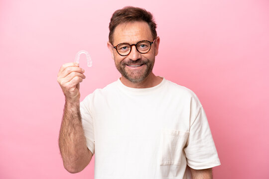 Middle age man holding invisible braces isolated on pink background smiling a lot