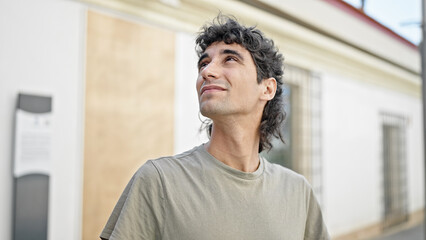 Young hispanic man looking to the sky with serious expression at street