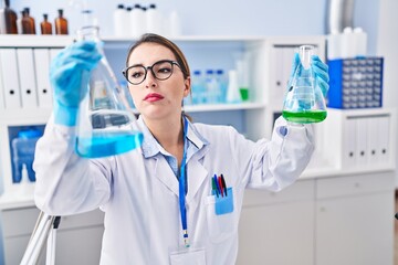 Young beautiful hispanic woman scientist holding test tubes at laboratory