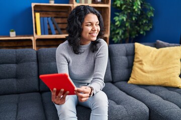 Young latin woman using touchpad sitting on sofa at home