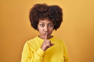 Fototapeta na wymiar Young african american woman standing over yellow background asking to be quiet with finger on lips. silence and secret concept.
