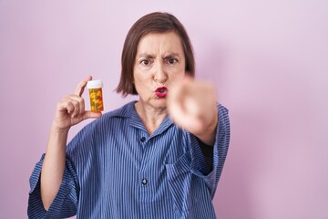 Middle age hispanic woman holding pills pointing with finger to the camera and to you, confident gesture looking serious