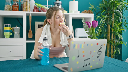 Fototapeta na wymiar Young blonde woman wearing sportswear using laptop eating apple at dinning room