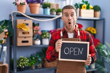 Young caucasian man working at florist holding open sign afraid and shocked with surprise and amazed expression, fear and excited face.