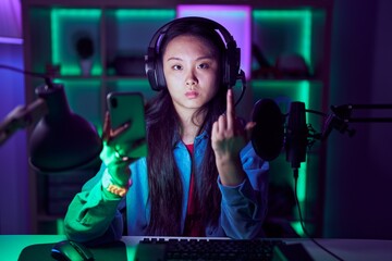 Young asian woman playing video games with smartphone showing middle finger, impolite and rude fuck...