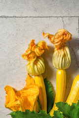 Fresh yellow zucchini or squash with flowers on sunlit background with shadows. Top view. Organic vegan food
