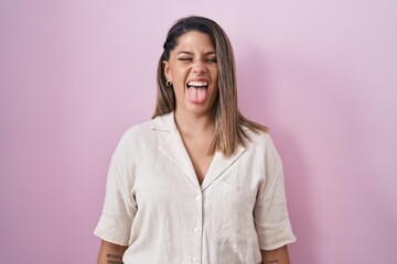 Blonde woman standing over pink background sticking tongue out happy with funny expression. emotion...