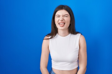 Young caucasian woman standing over blue background sticking tongue out happy with funny expression. emotion concept.