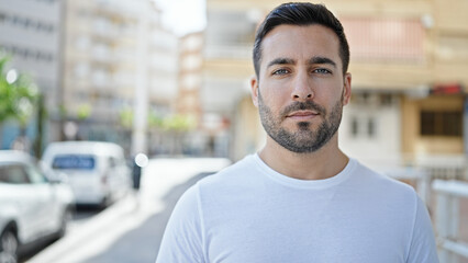 Young hispanic man standing with serious expression at street