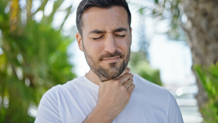 Young hispanic man standing with serious expression being sick at park