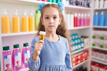 Young little girl holding pills at the pharmacy thinking attitude and sober expression looking self confident
